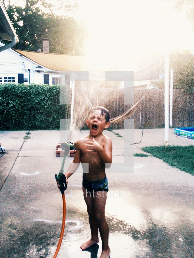 Boy playing in the sprinkler outside.