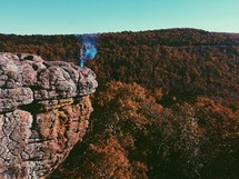 a man and blue smoke at the edge of a cliff 