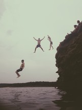 men jumping off a cliff into water