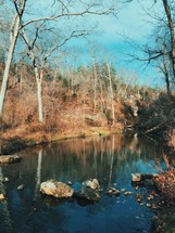 A calm stream reflecting surrounding trees.