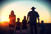 Family in westernwear standing in field at sunset.