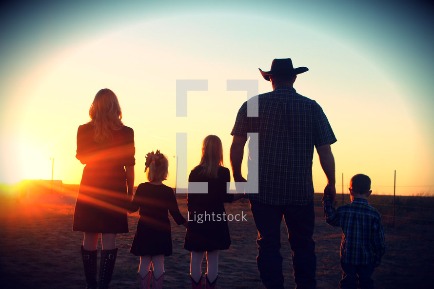 Family in westernwear standing in field at sunset.