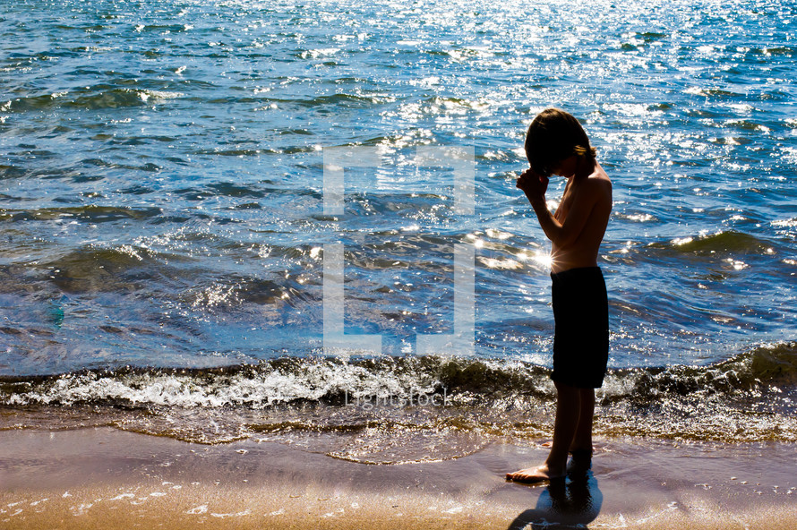 Boy praying on the beach.