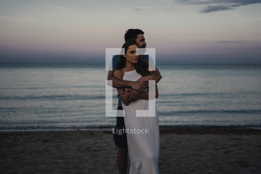 Man holding woman in white dress by the beach