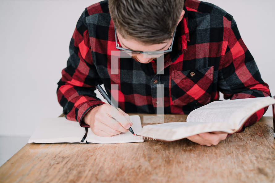 man writing in a journal and reading a Bible 