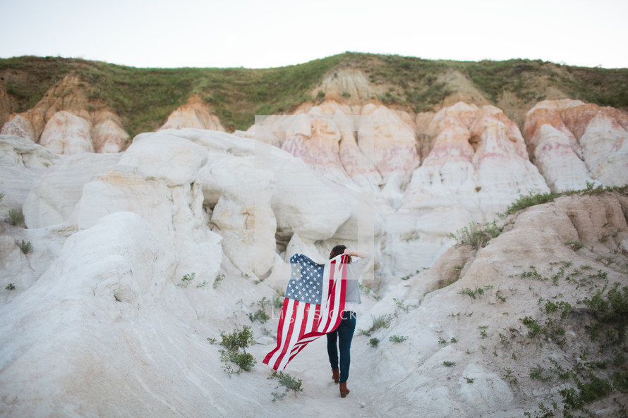  a woman walking carrying an American flag on her back 