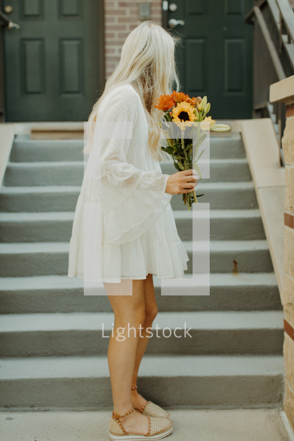 a blonde woman standing outdoors holding flowers 
