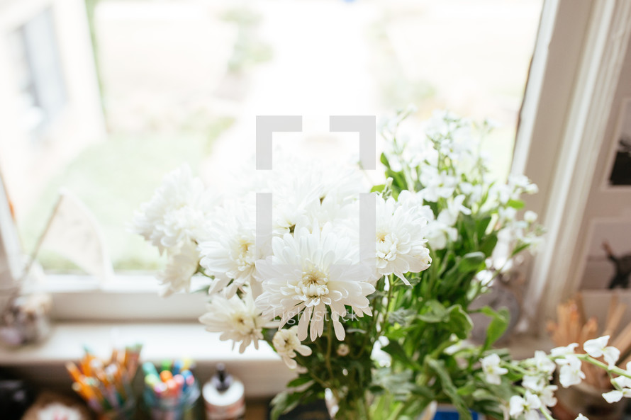 flowers in a vase on a desk in front of a window 