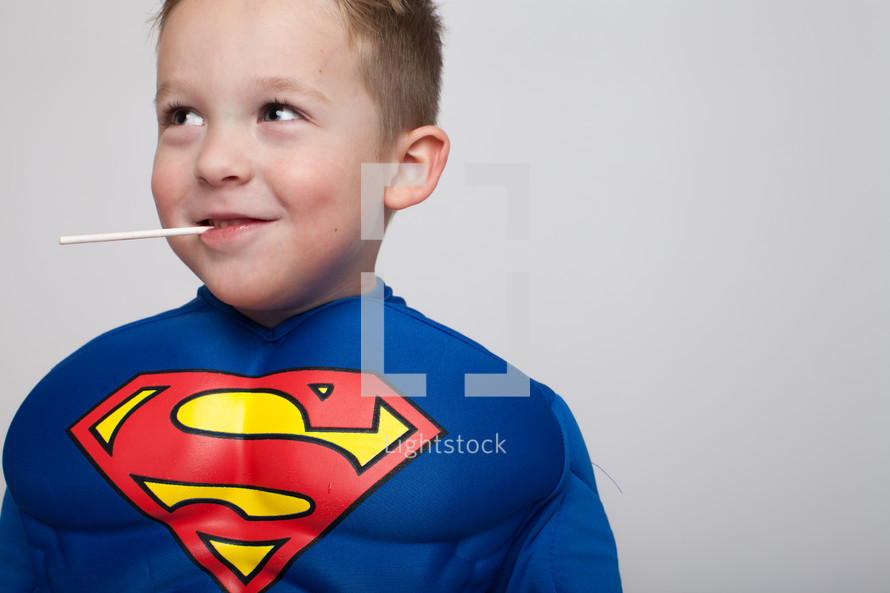 a boy child in a superman costume with a sucker in his mouth 