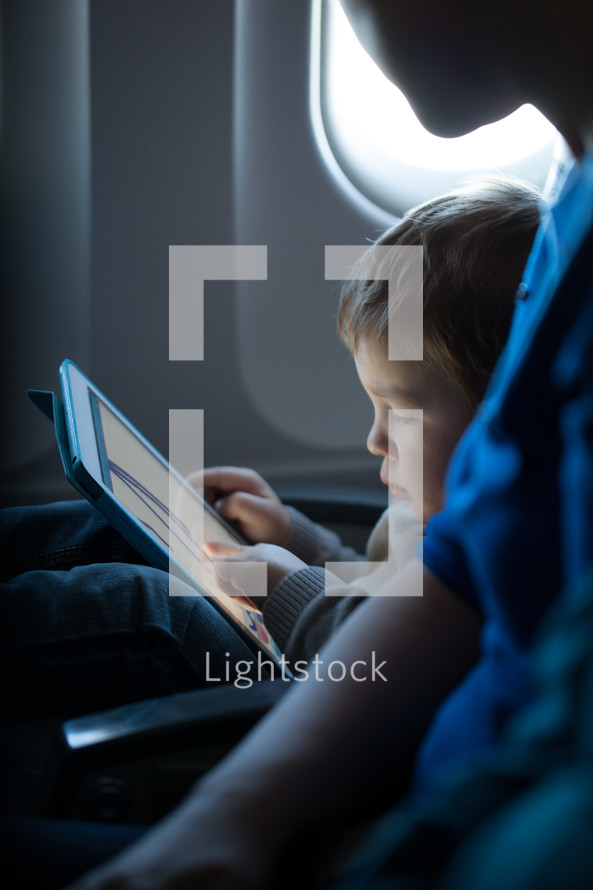 Little boy playing with a tablet in an airplane