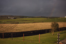 farmland under a gray sky with rainbow 