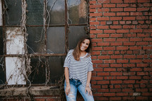 a young woman leaning on the wall of an old brick warehouse 