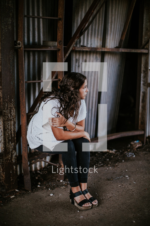 a young woman sitting on a rusty ladder 