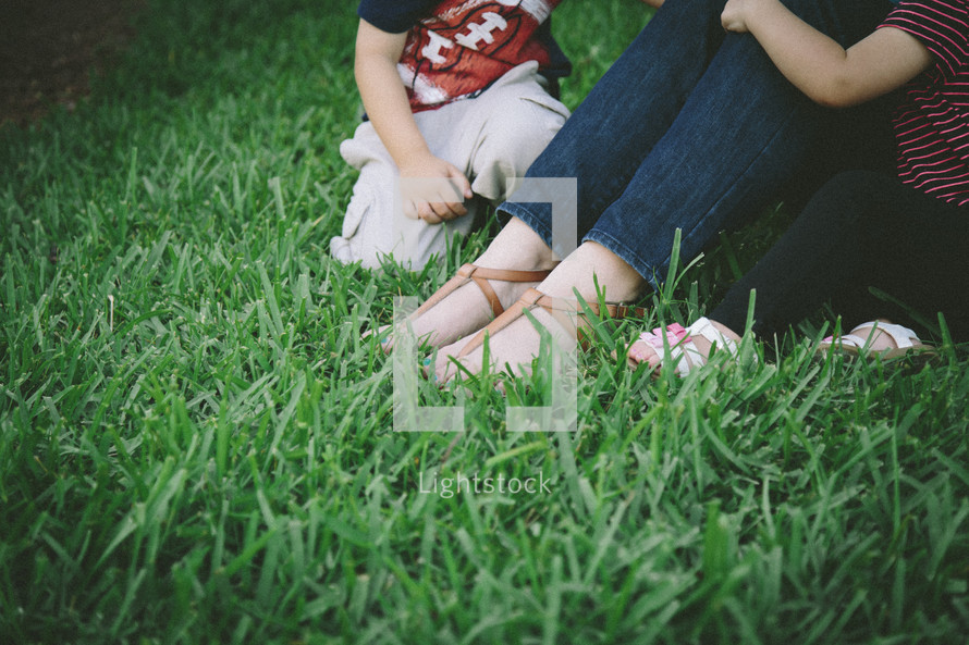 Children sitting in the grass with their mother.