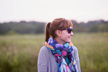a woman in a scarf and sunglasses standing in a field 