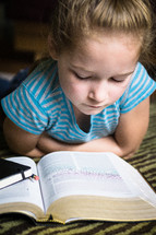 A young girl laying on the floor and reading the Bible.