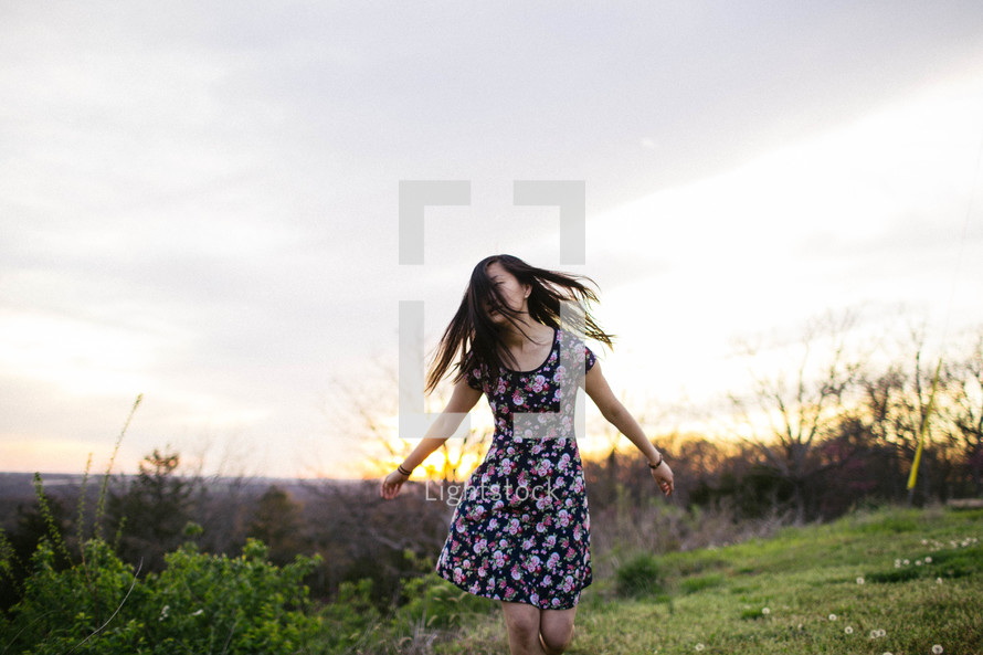 a girl walking in a meadow at sunset 