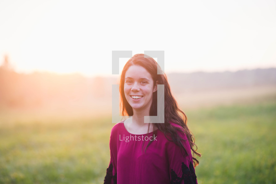 a woman standing alone in a meadow at sunrise 