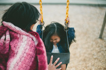 A woman pushes a little girl on a swing.
