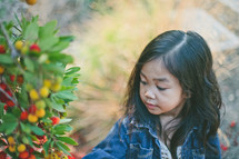 A little girl looks at a bush full of berries.