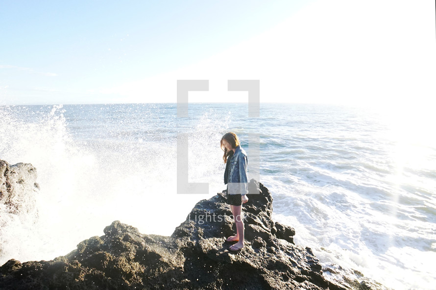 girl standing on rocks with waves splashing her 