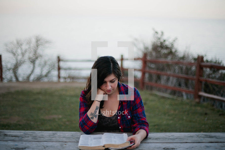 Woman reading the Bible at an outdoor picnic table.