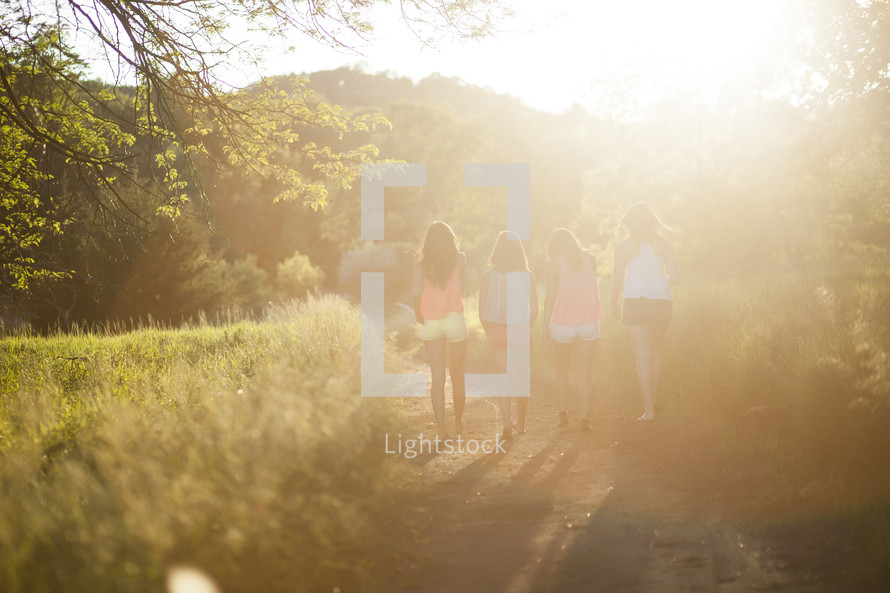 sunlight shining on a dirt path and girls walking down it 
