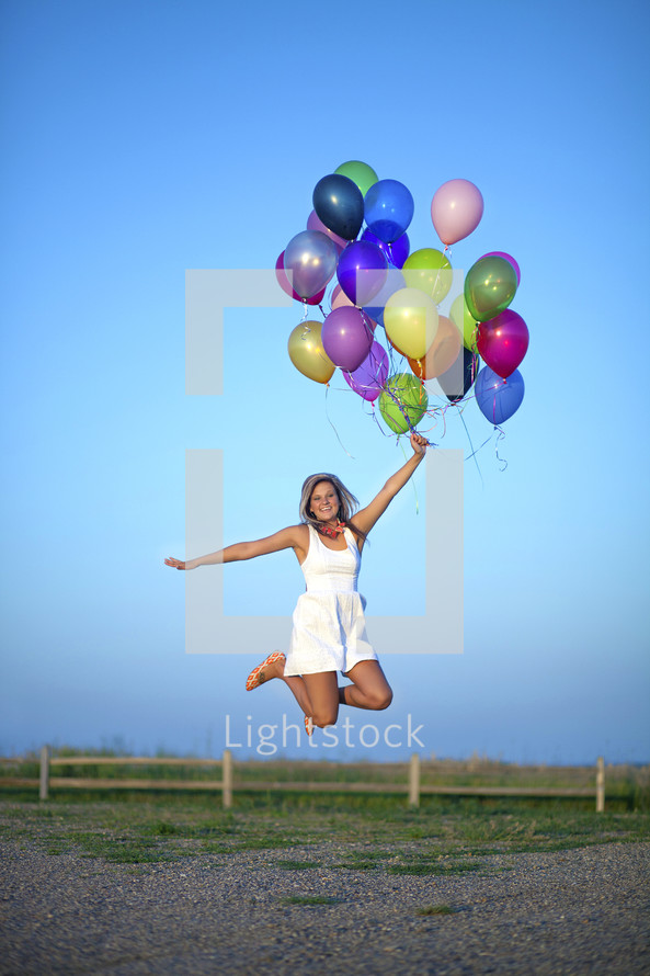 a woman jumping in celebration holding helium balloons 