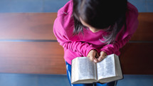 a girl sitting on a bench reading a Bible 