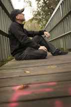 a man sitting on a boardwalk thinking and looking up at the sky 