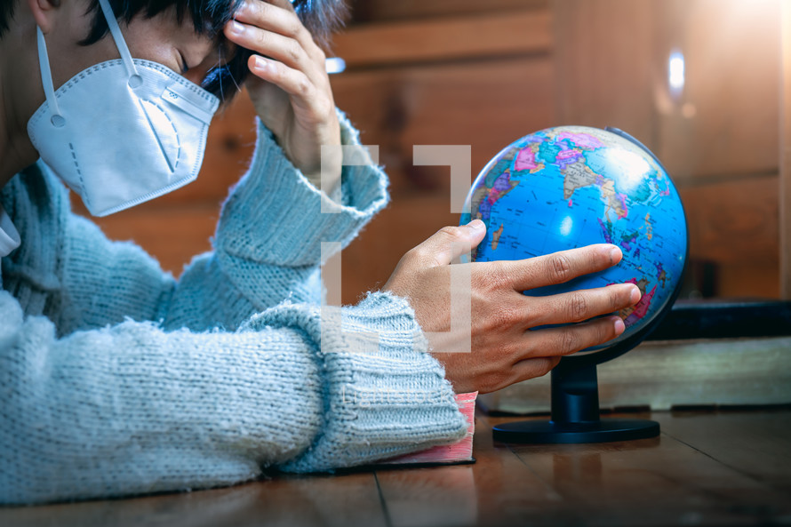 person wearing a face mask with praying hands beside of a globe 
