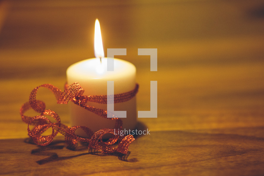flame on a white candle wrapped in red ribbon 