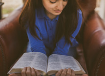 A woman sitting in a leather chair reading a Bible 