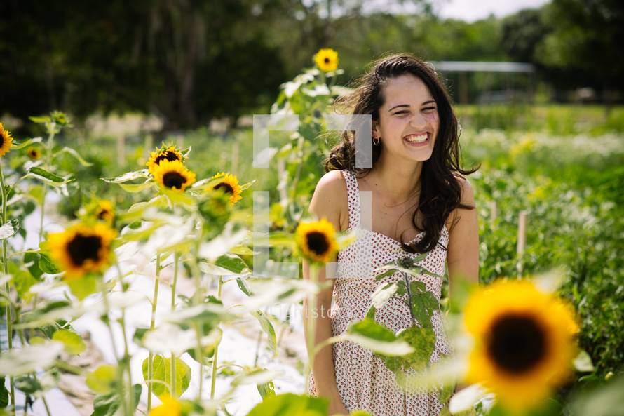 A smiling young woman in a field of sunflowers.