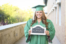 A graduate holding a thanks mom and dad sign 
