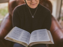 Woman reading the Bible while sitting in a chair.