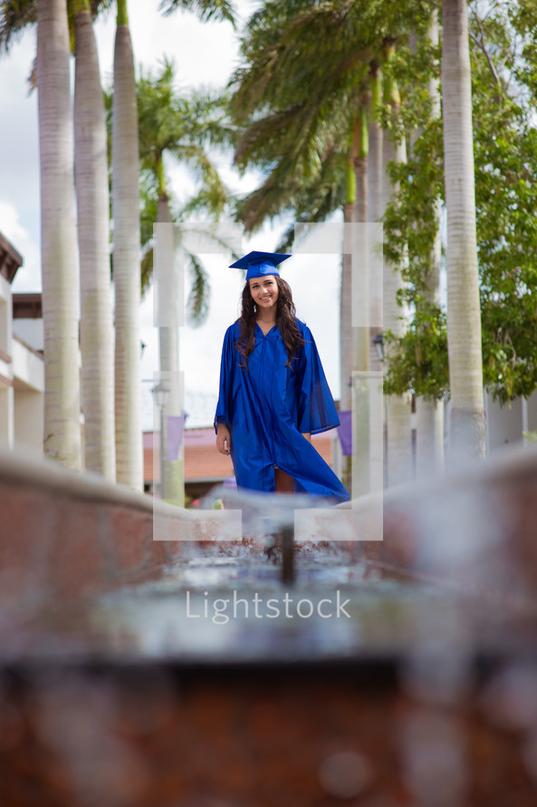 a graduate in cap and gown standing under palm trees 