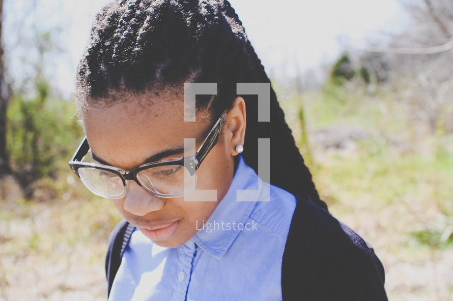 an African American teen girl in reading glasses looking down 