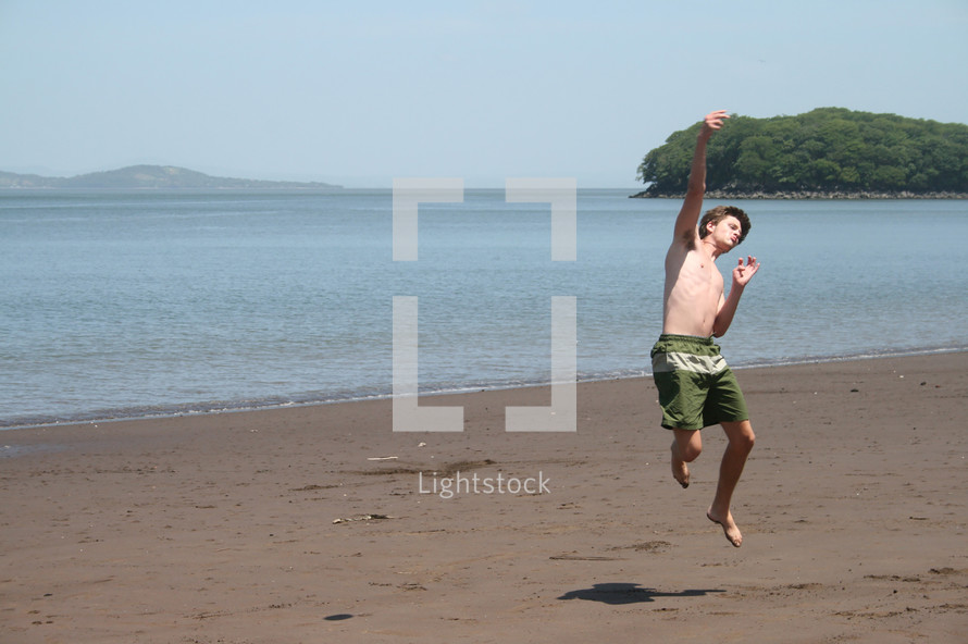 teen boy jumping for joy on a beach 
