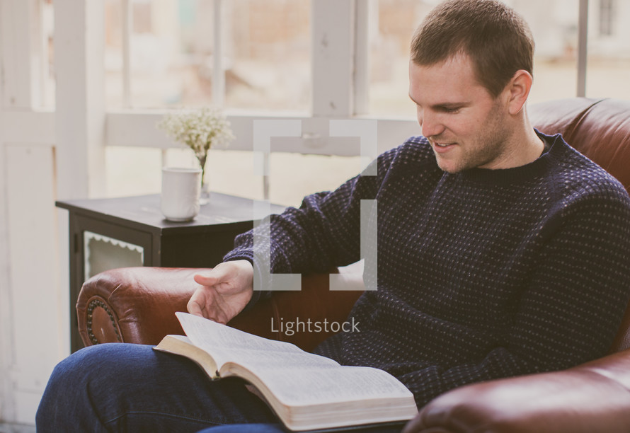 A man sitting in a chair reading a Bible 