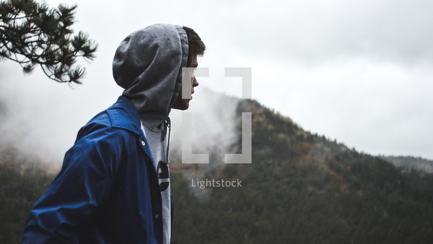man in a hoodie looking out at a mountain 