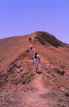 people walking up desert sand dunes 