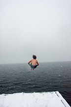A teen doing a cannonball into the ocean in the winter.