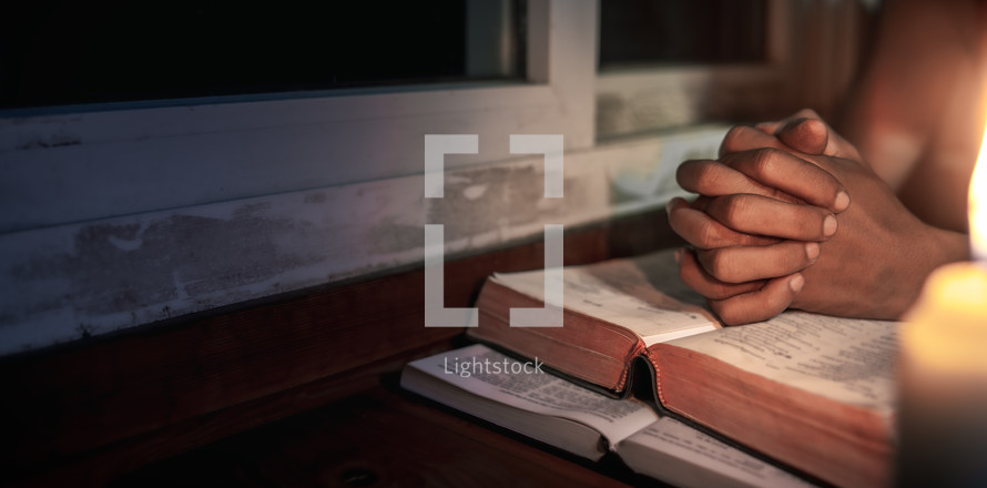 Bible with candlelight and praying hands
