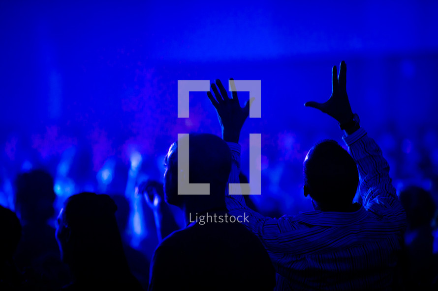 audience under blue light with hands raised 