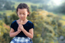 a girl holding a cross praying outdoors 
