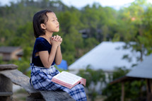 a girl praying with a Bible outdoors 