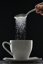 Tea cup or coffee and pouring sugar spoon on black background