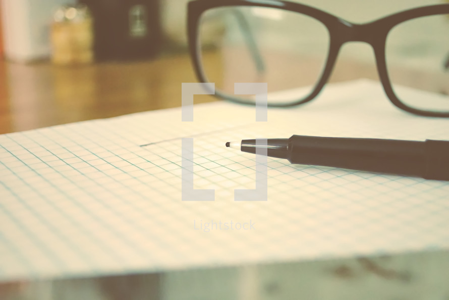 pen and reading glasses on graph paper 