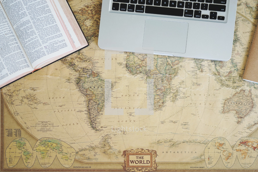 Bible, laptop, and journal on a world map 